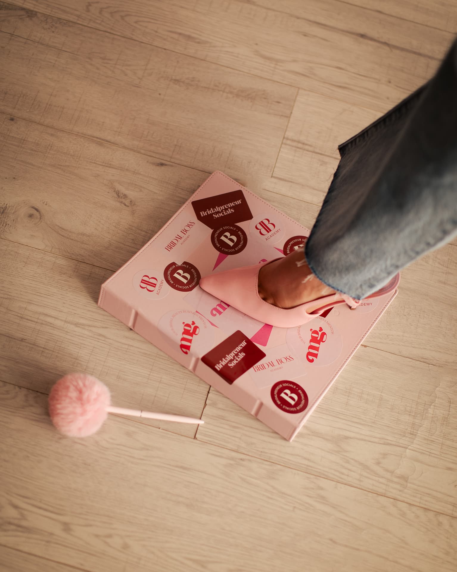 A pink heel stepping on a Bridal Boss Academy folder